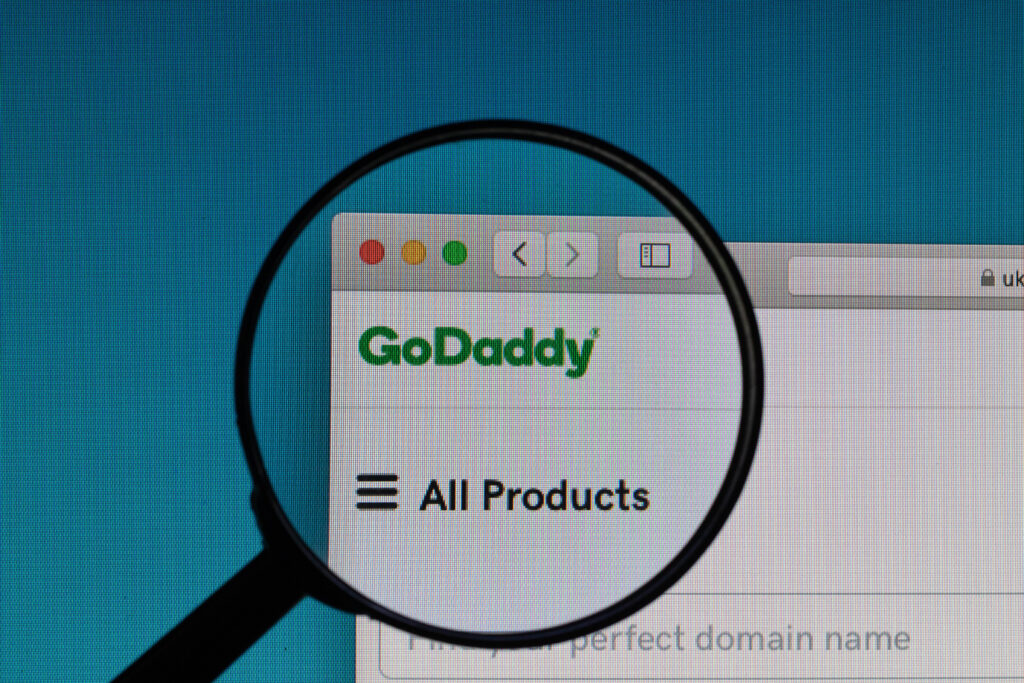 an image of Godaddy logo under magnifying glass for article  What to Do After Buying a Domain Name from GoDaddy?